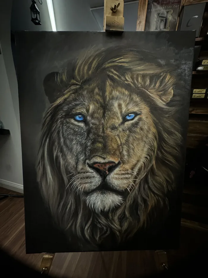 Photorealistic A2 oil painting of a lion with blue eyes on dark background by Esther, Unicorn Tattoo Art Collective, Ashford Surrey