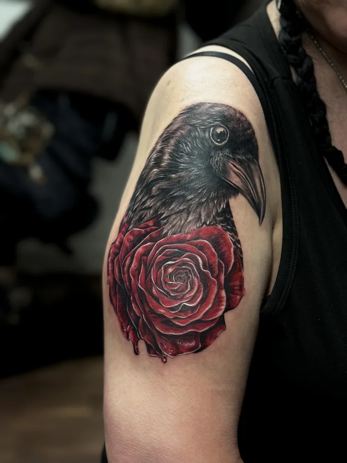 Realistic black and grey raven with red rose cover up tattoo on upper arm by Esther at Unicorn Tattoo Art Collective, Ashford Surrey