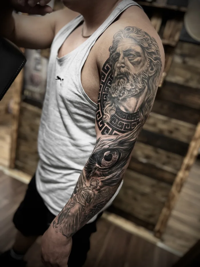 Black and grey realistic Greek god full sleeve tattoo with eye and angel details on arm by Esther at Unicorn Tattoo Art Collective in Ashford Surrey