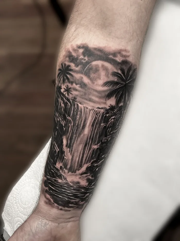 Black and Grey waterfall forearm tattoo with palm trees and moon at Unicorn Tattoo Art Collective in Ashford  Surrey