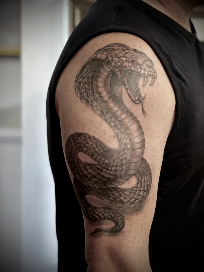 Realistic snake tattoo, black and grey upper arm with detailed scale work, \Unicorn Tattoo Art Collective Ashford Surrey.