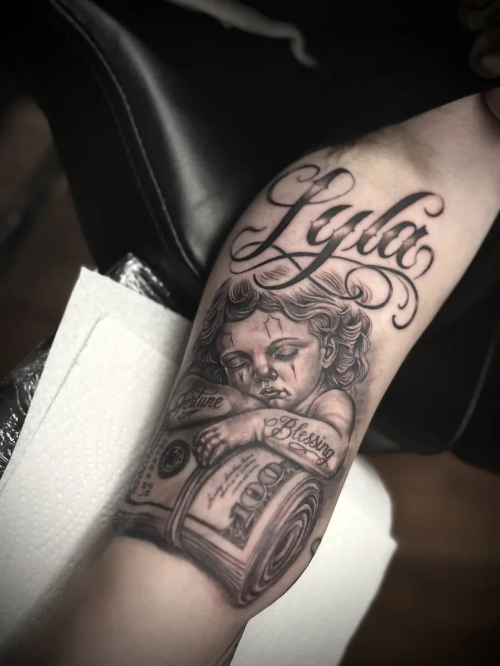 Black and grey realistic cherub and script tattoo by Esther at Unicorn Tattoo Art Collective in Ashford, Surrey