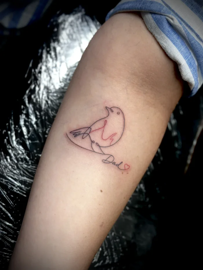 Fine line memorial tattoo by Esther at Unicorn Tattoo Art Collective in Ashford, Surrey, featuring a small bird, Dad script and red heart detail