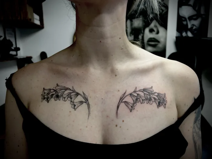 Fine line floral collarbone tattoo by Esther at Unicorn Tattoo Art Collective in Ashford, Surrey, featuring delicate botanical flowers across the upper chest