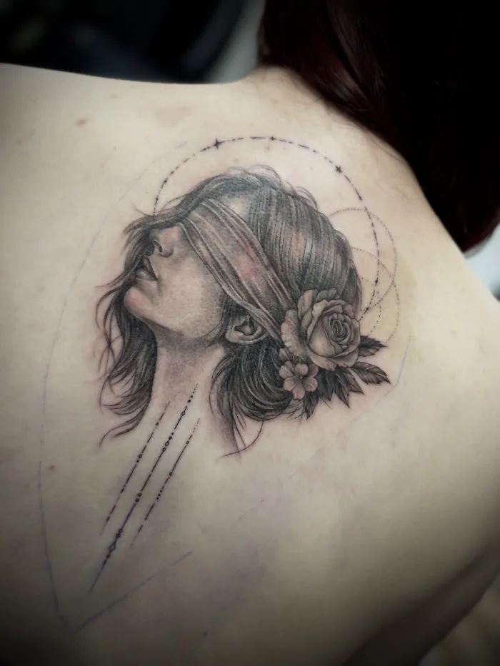 Black and grey back tattoo with female portrait, floral detail and fine line elements by Esther at Unicorn Tattoo Art Collective in Ashford, Surrey
