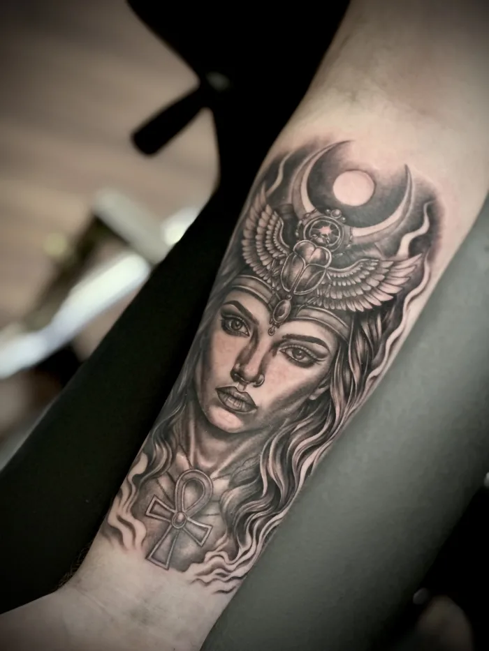 Black and grey Egyptian-style female portrait forearm tattoo with winged scarab, moon and ankh by Esther in Ashford, Surrey